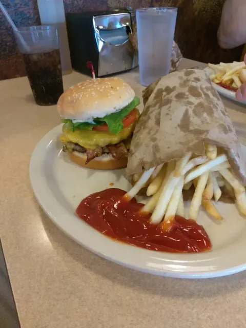 Burger, fries, and ketchup on a plate, with a soft drink and water glass.