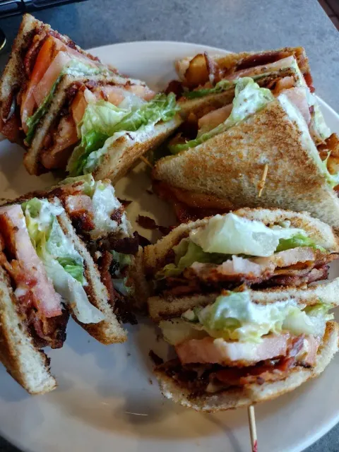 Club sandwiches, stacked high with bacon, lettuce, tomato, and turkey, on a plate.