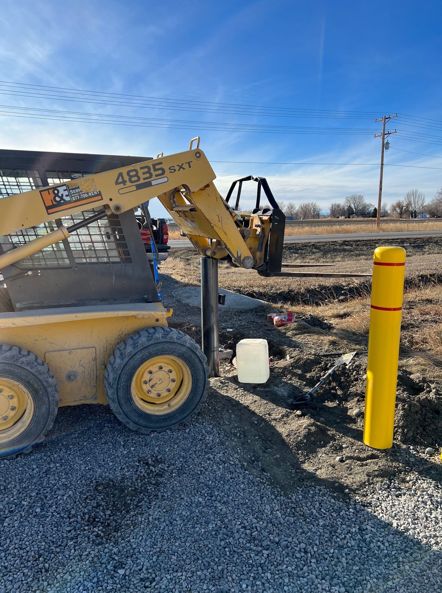 A yellow tractor is parked next to a yellow pole on a gravel road.