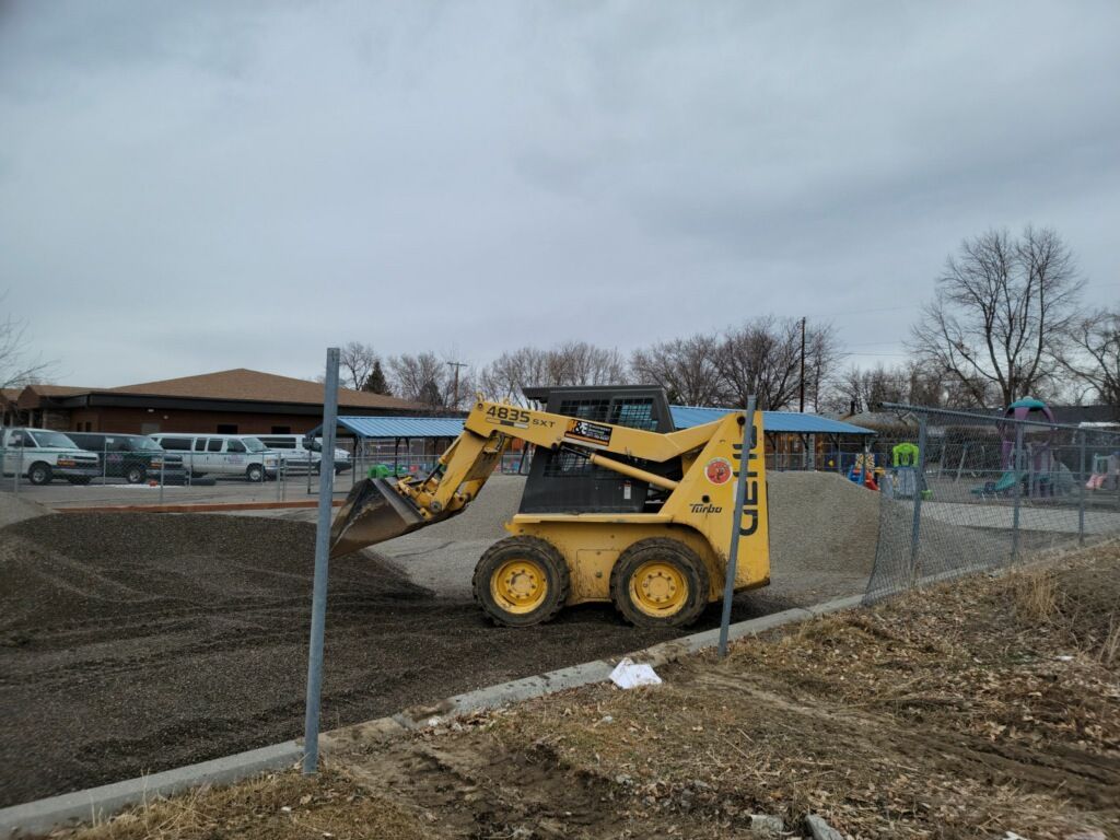 A yellow bulldozer is sitting on top of a dirt field next to a fence.