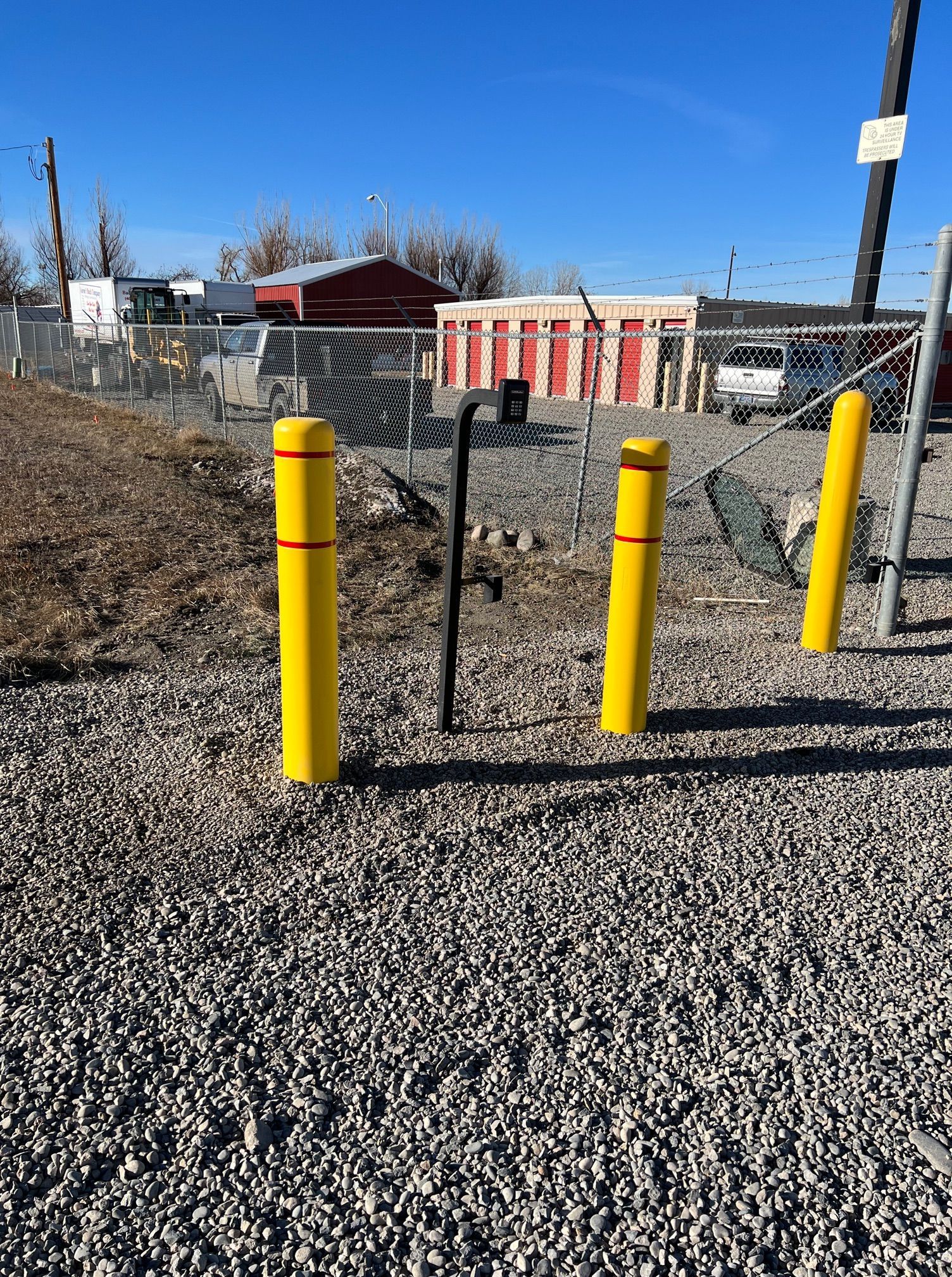 A gravel area with yellow poles and a chain link fence.