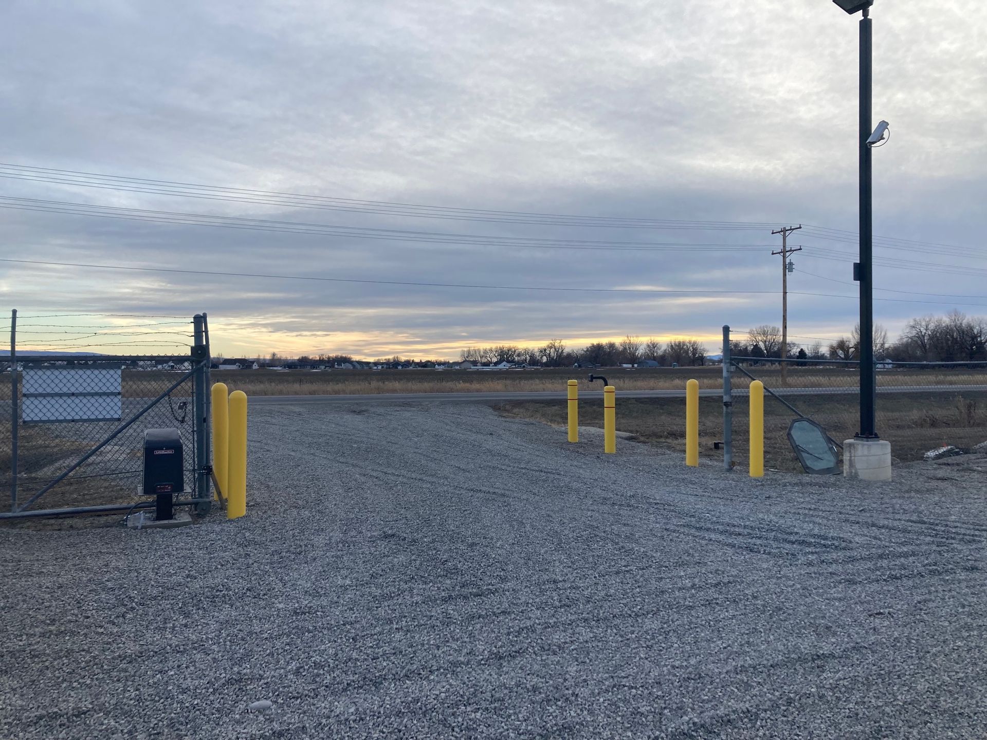A gravel road with a gate and yellow poles on the side of it.