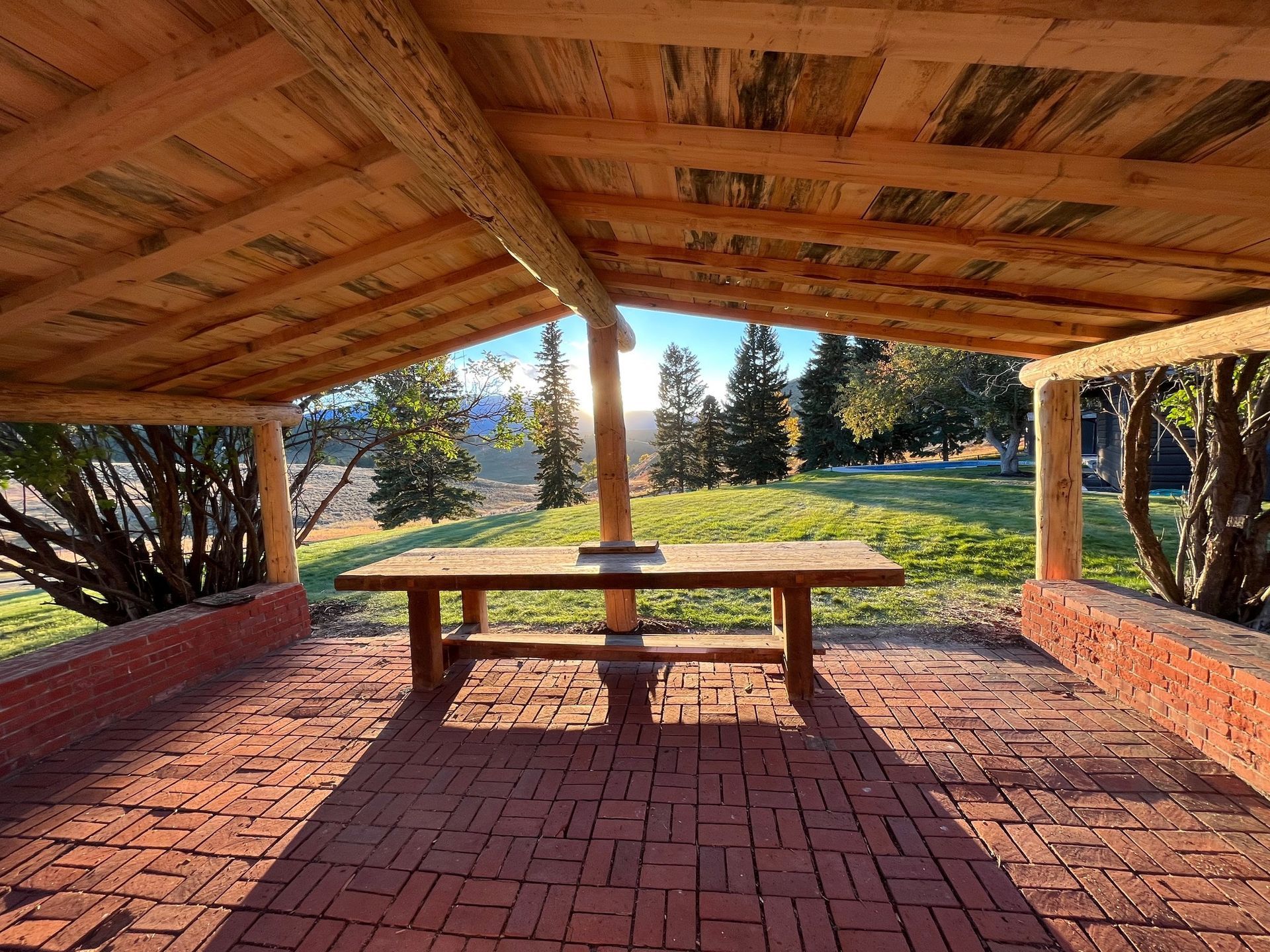 A wooden picnic table is under a wooden roof.