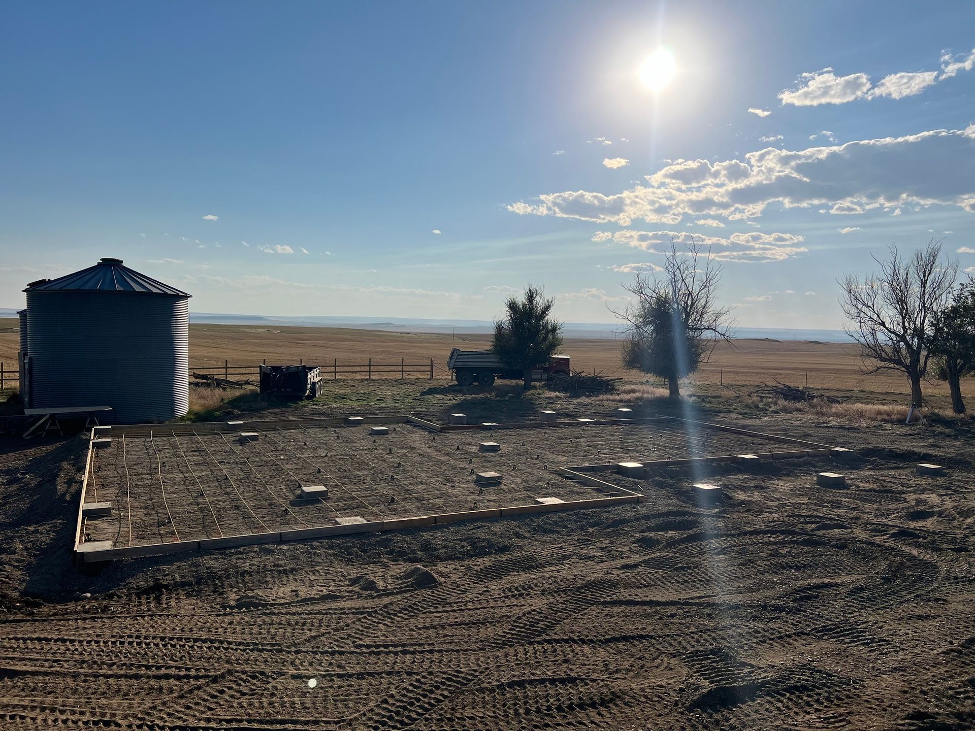The sun is shining through the clouds over a dirt field with a silo in the background.