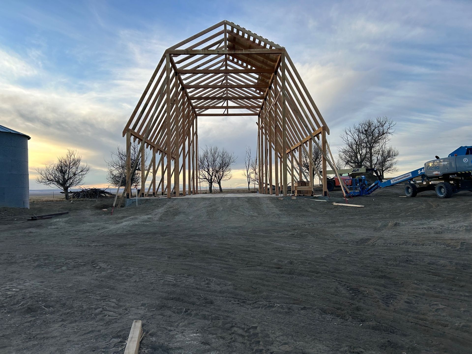 A large wooden barn is being built in a dirt field.