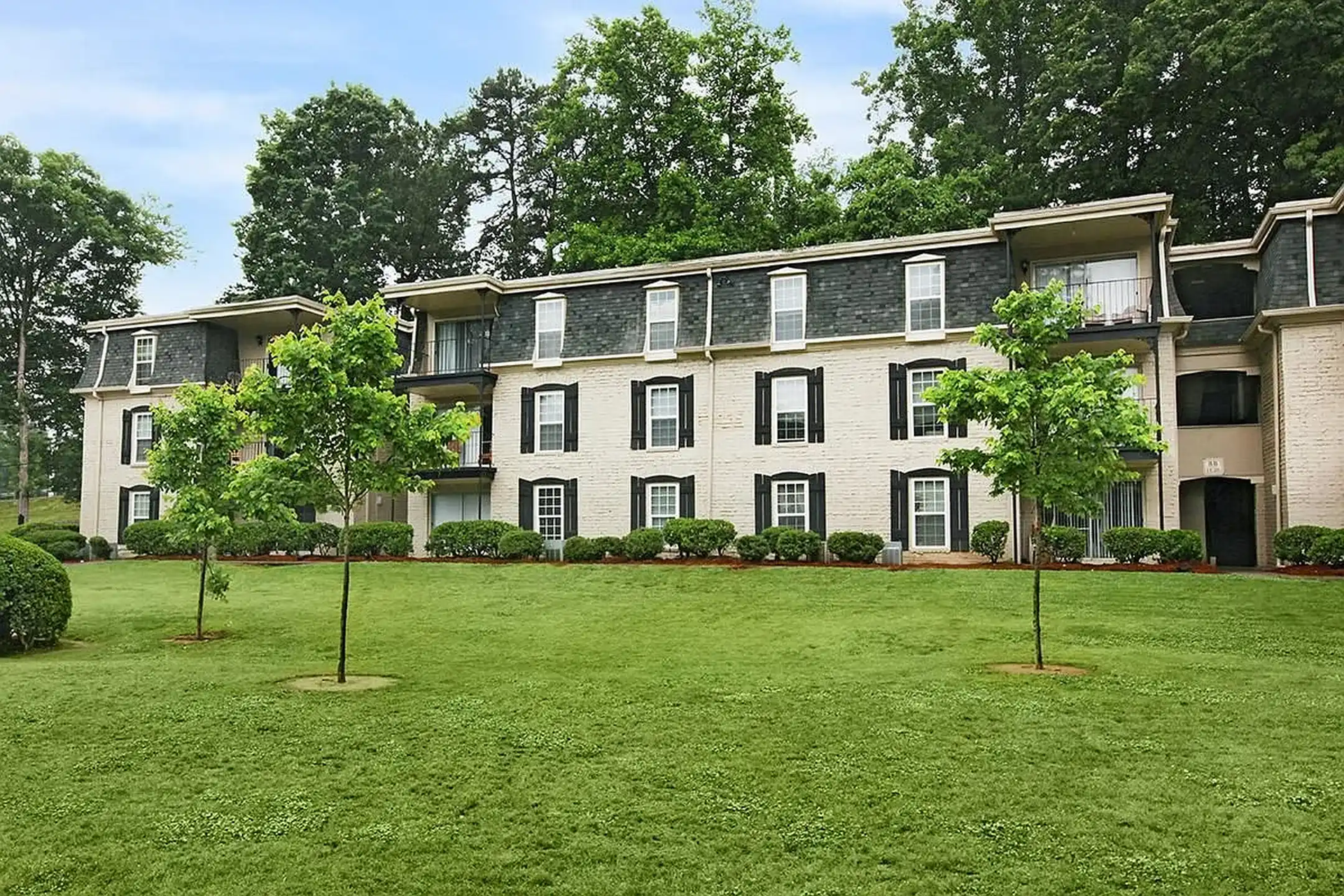 White apartment building with dark shutters behind a green lawn and small trees