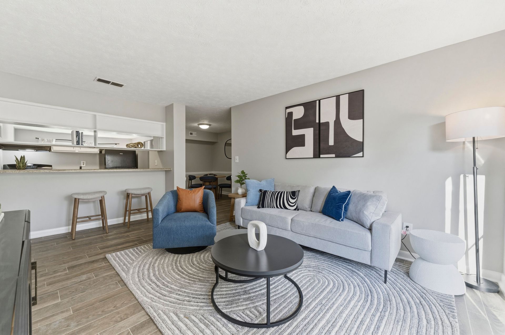 Bright modern living room with gray sofa, blue chair, patterned rug, and open kitchen bar stools