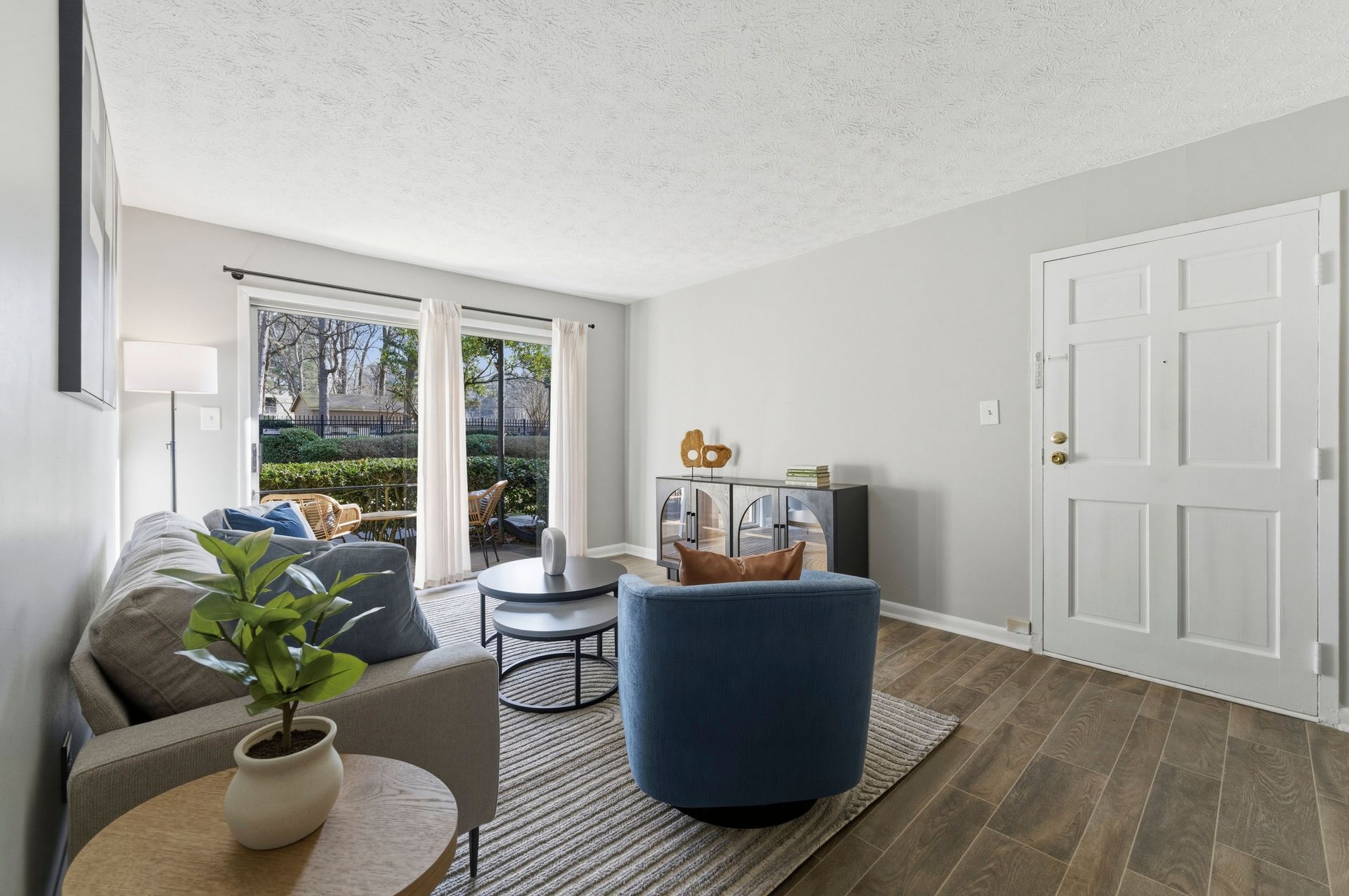 Bright living room with gray sofa, blue chair, plant, coffee table, and sliding glass doors to a patio.