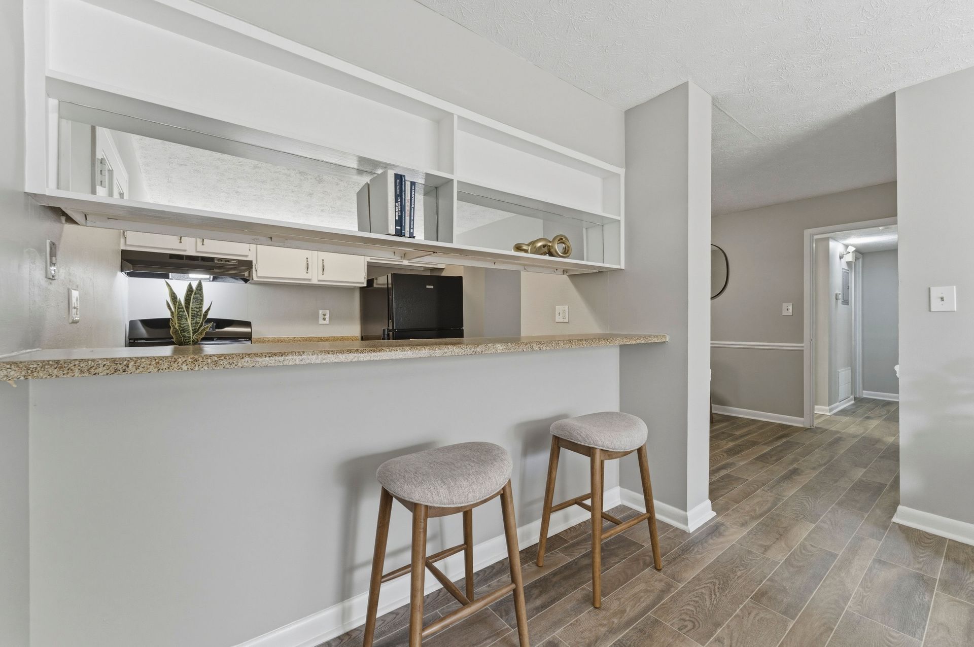Bright modern kitchen pass-through with two stools, white cabinets, granite counter, and wood-look flooring