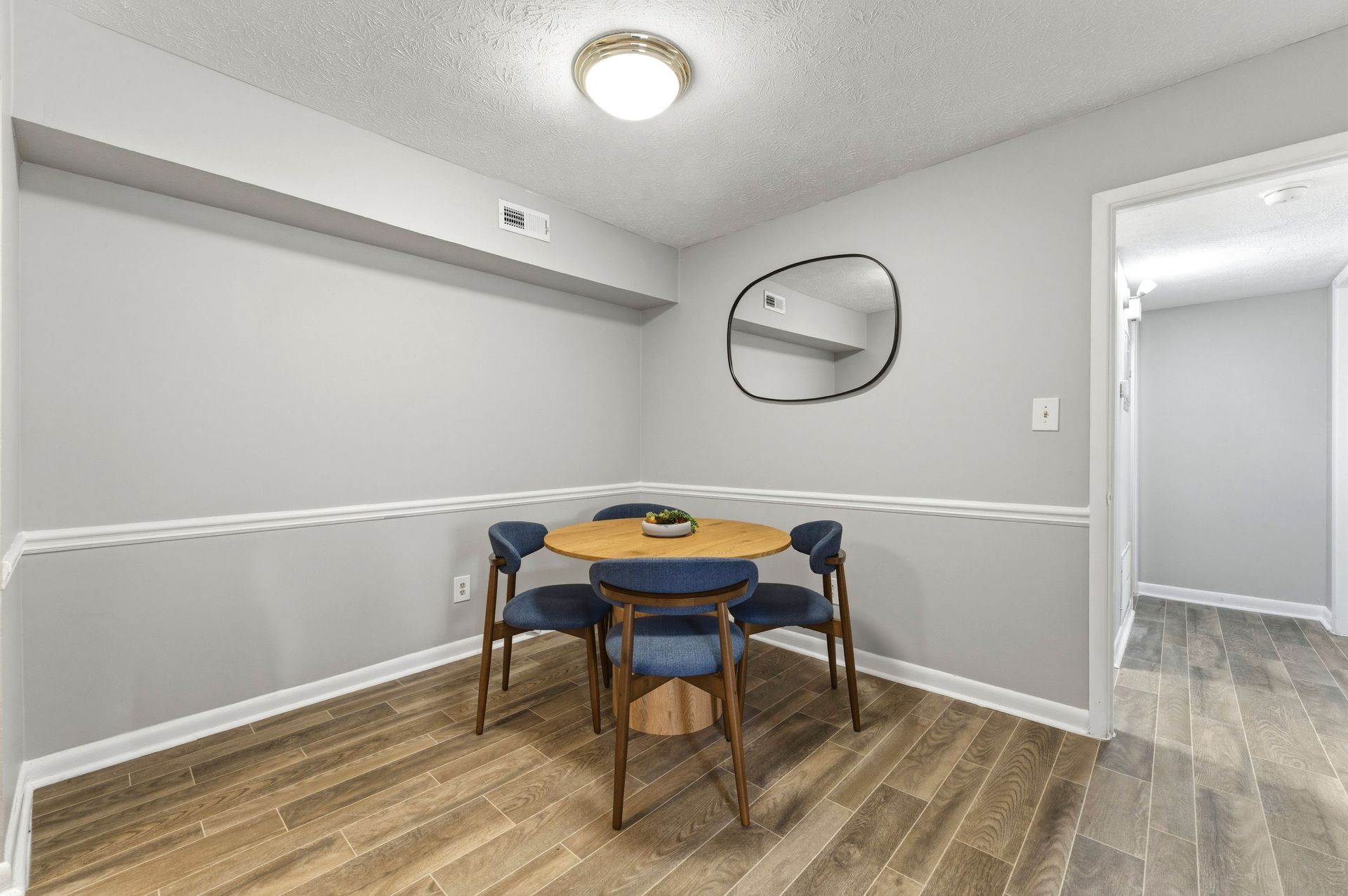 Modern dining area with wooden table, teal chairs, pendant lights, and an open kitchen with white cabinets.