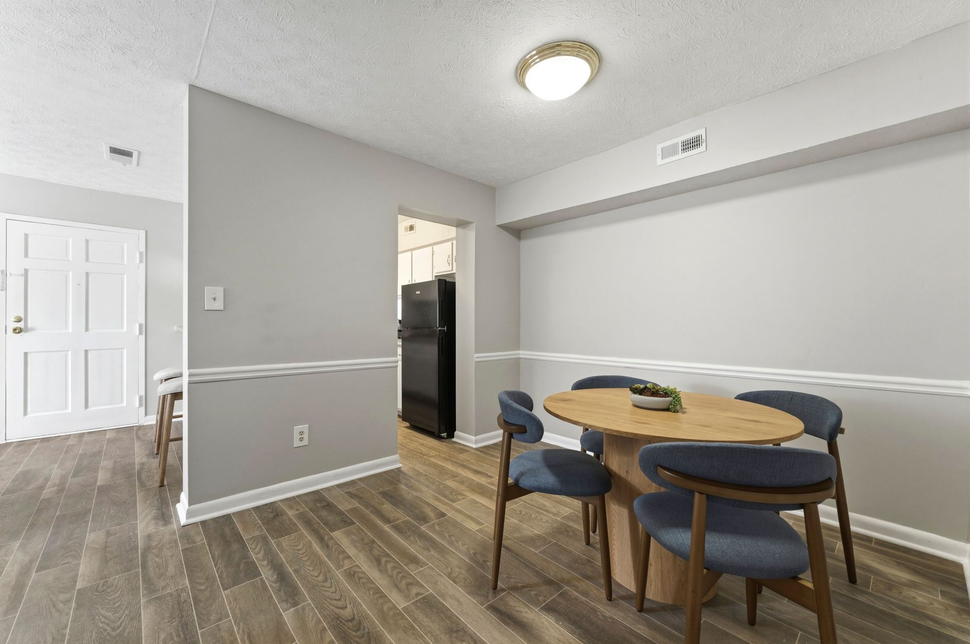Empty dining area with round table, blue chairs, gray walls, and wood-look flooring.