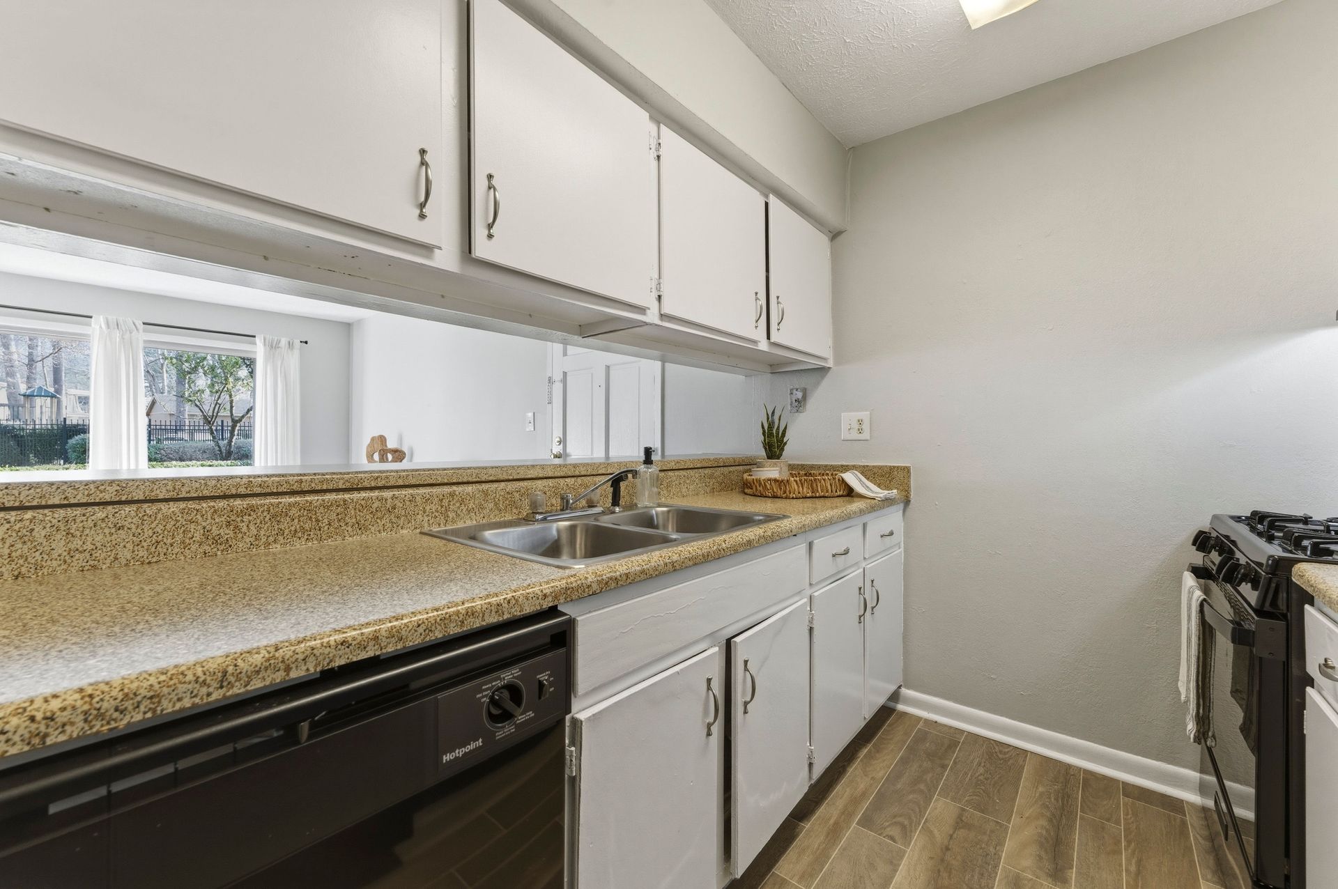 Bright kitchen with white cabinets, speckled countertops, and a gas stove beside a window.