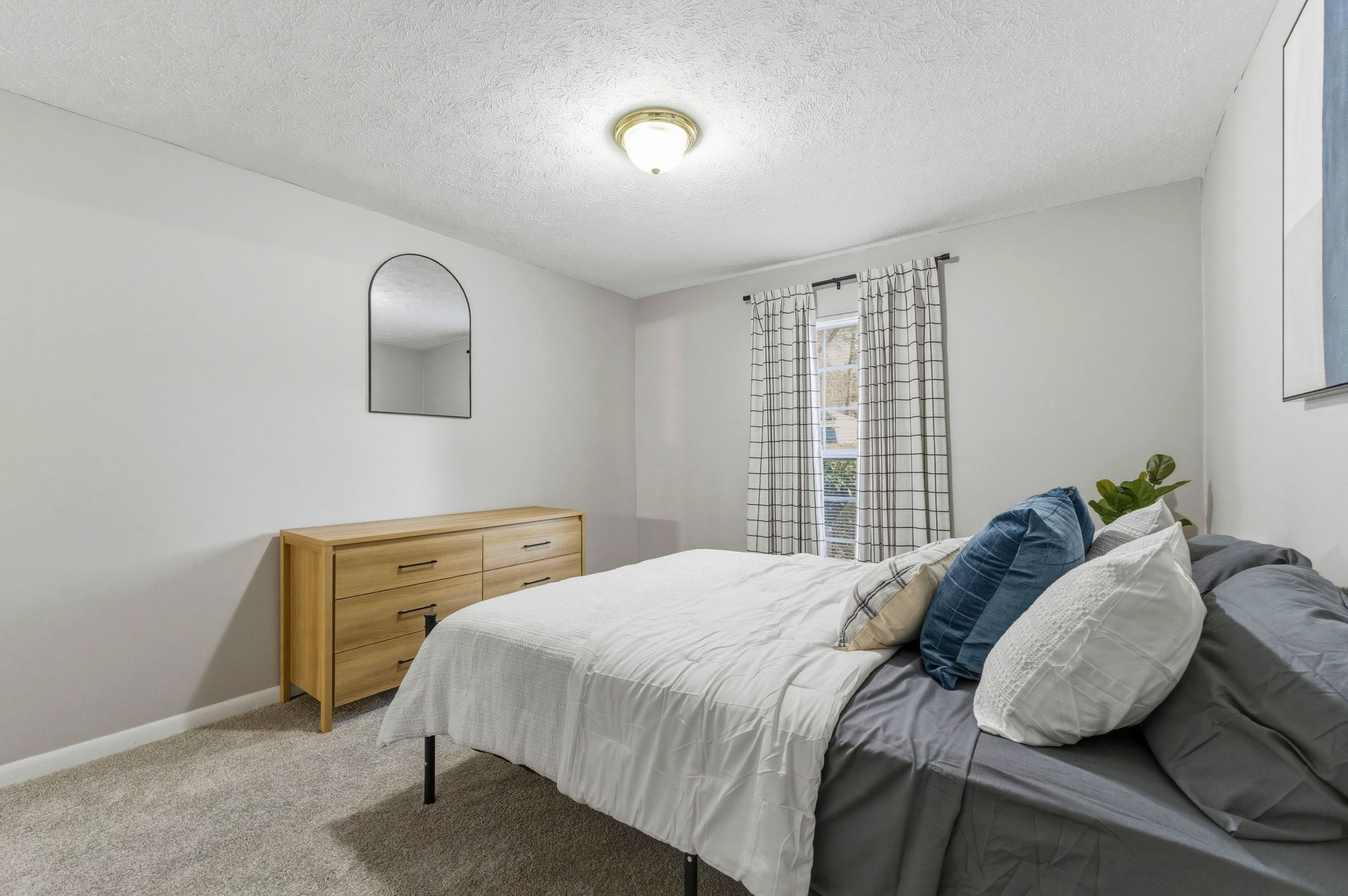 Bright bedroom with a bed, wooden dresser, and window with patterned curtains
