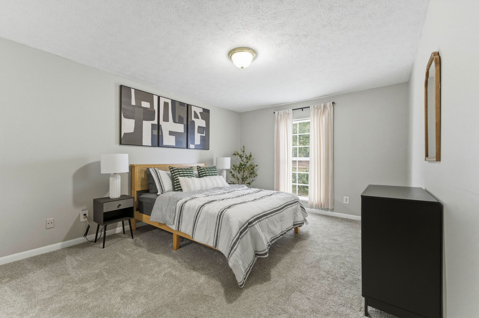 Bright bedroom with a bed, nightstands, dresser, gray carpet, and a window with curtains.
