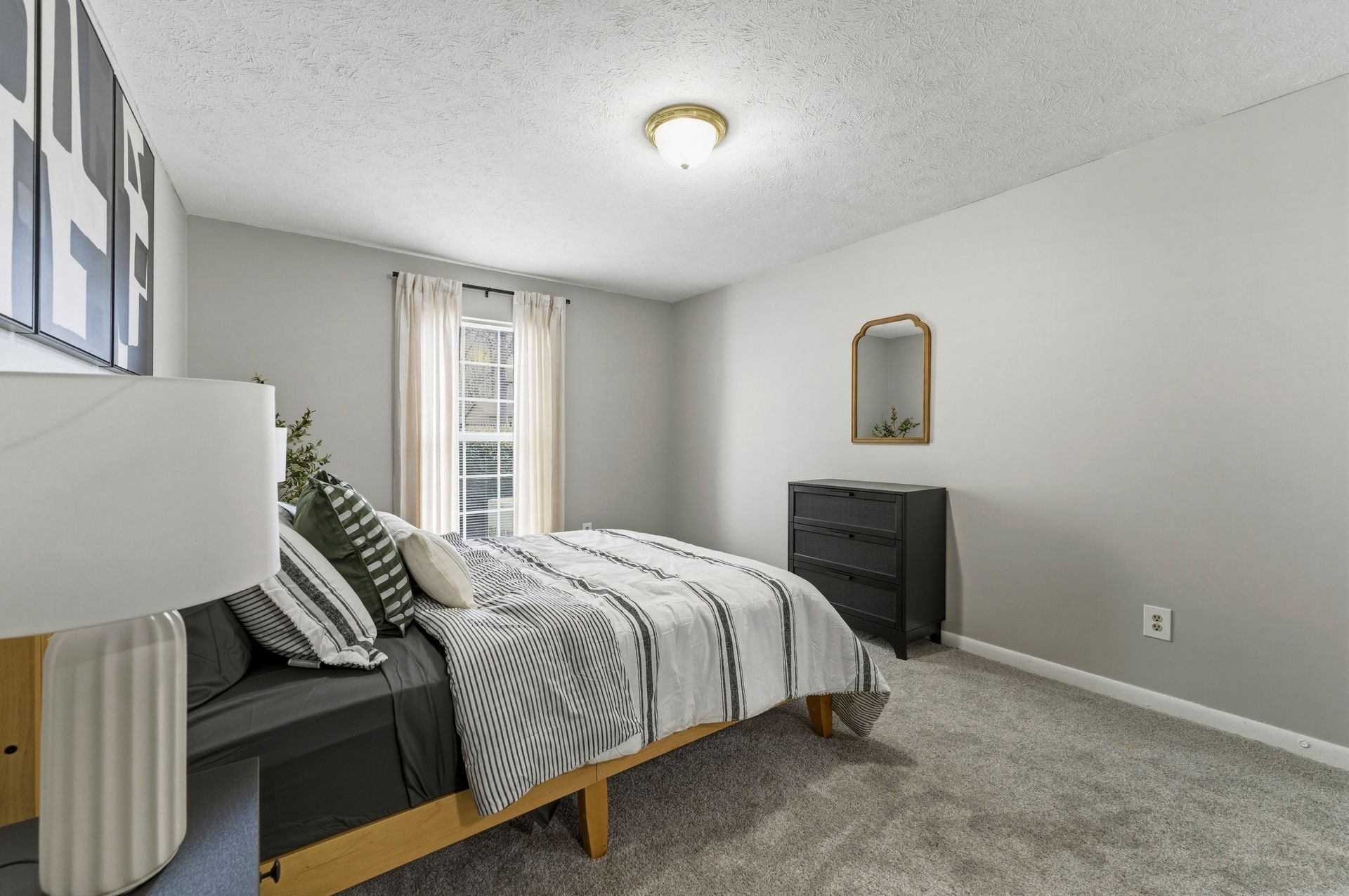 Minimal bedroom with twin bed, black dresser, window, and gray carpet.