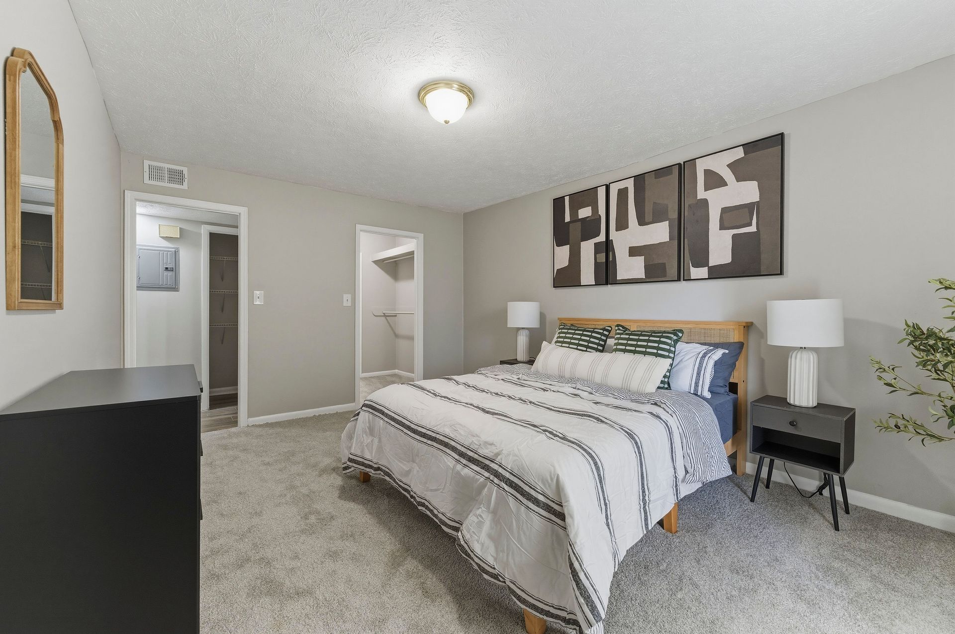 Bedroom with a made bed, nightstands, abstract wall art, and carpeted floor.