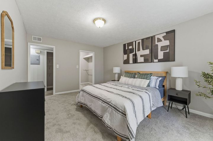 Bedroom with a made bed, nightstands, abstract wall art, and carpeted floor.