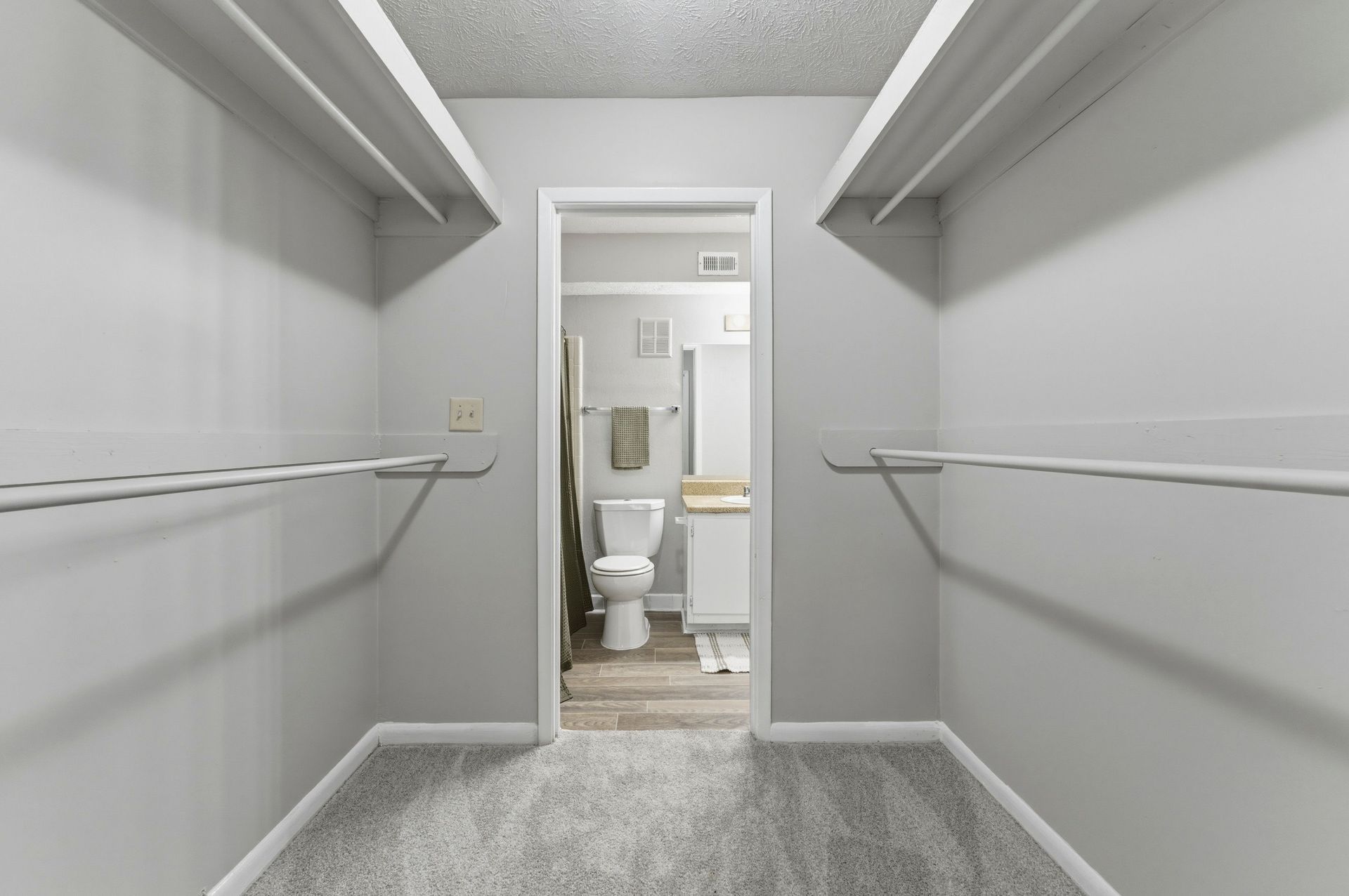Walk-in closet with shelves and hanging rods, looking into a small bathroom with a toilet and sink.