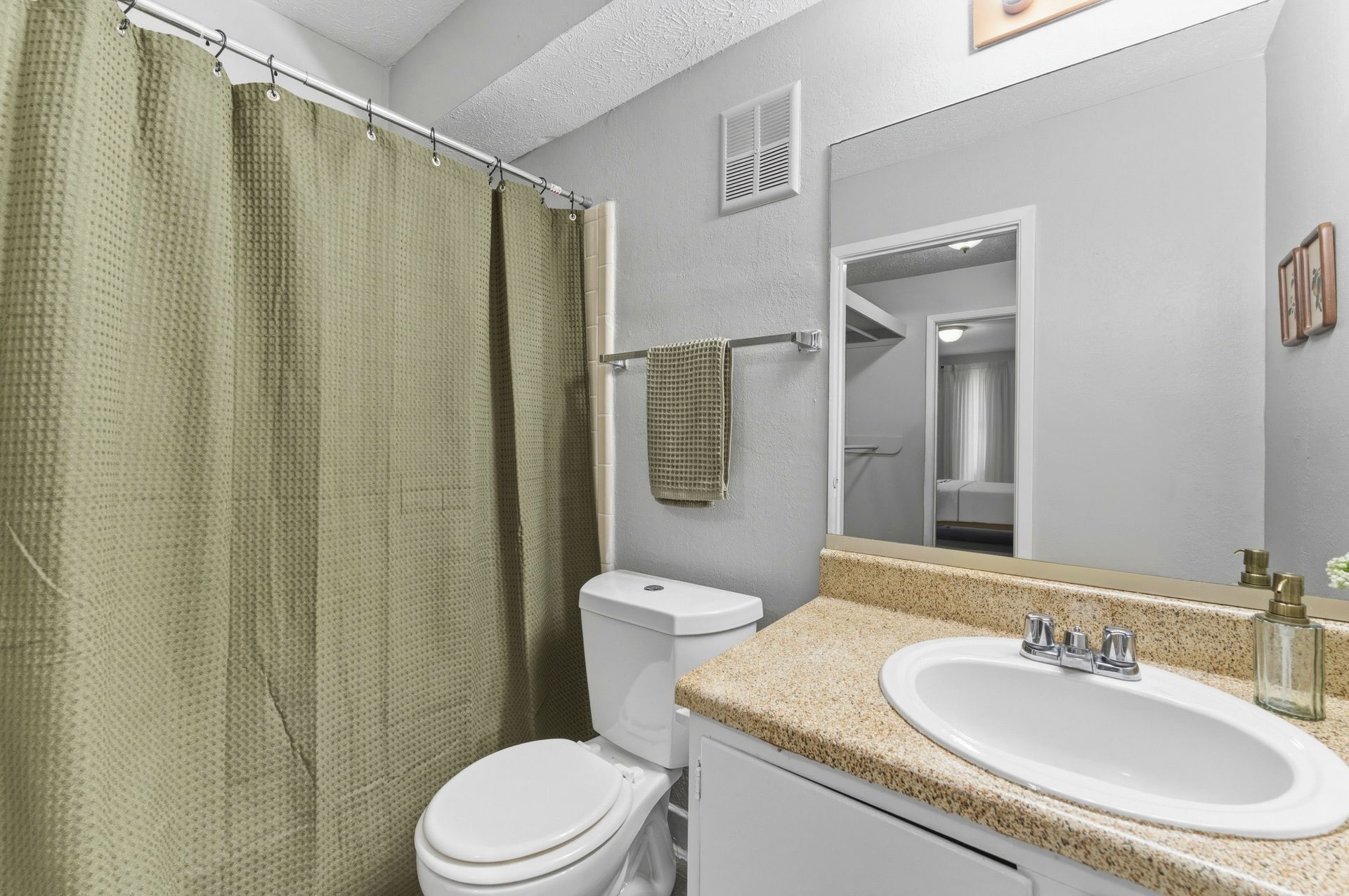 Small bathroom with beige shower curtain, white toilet, and granite countertop sink.