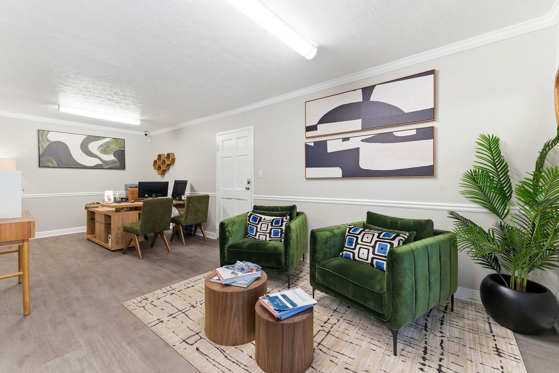 Modern living room with green chairs, wooden tables, large wall art, and a potted plant