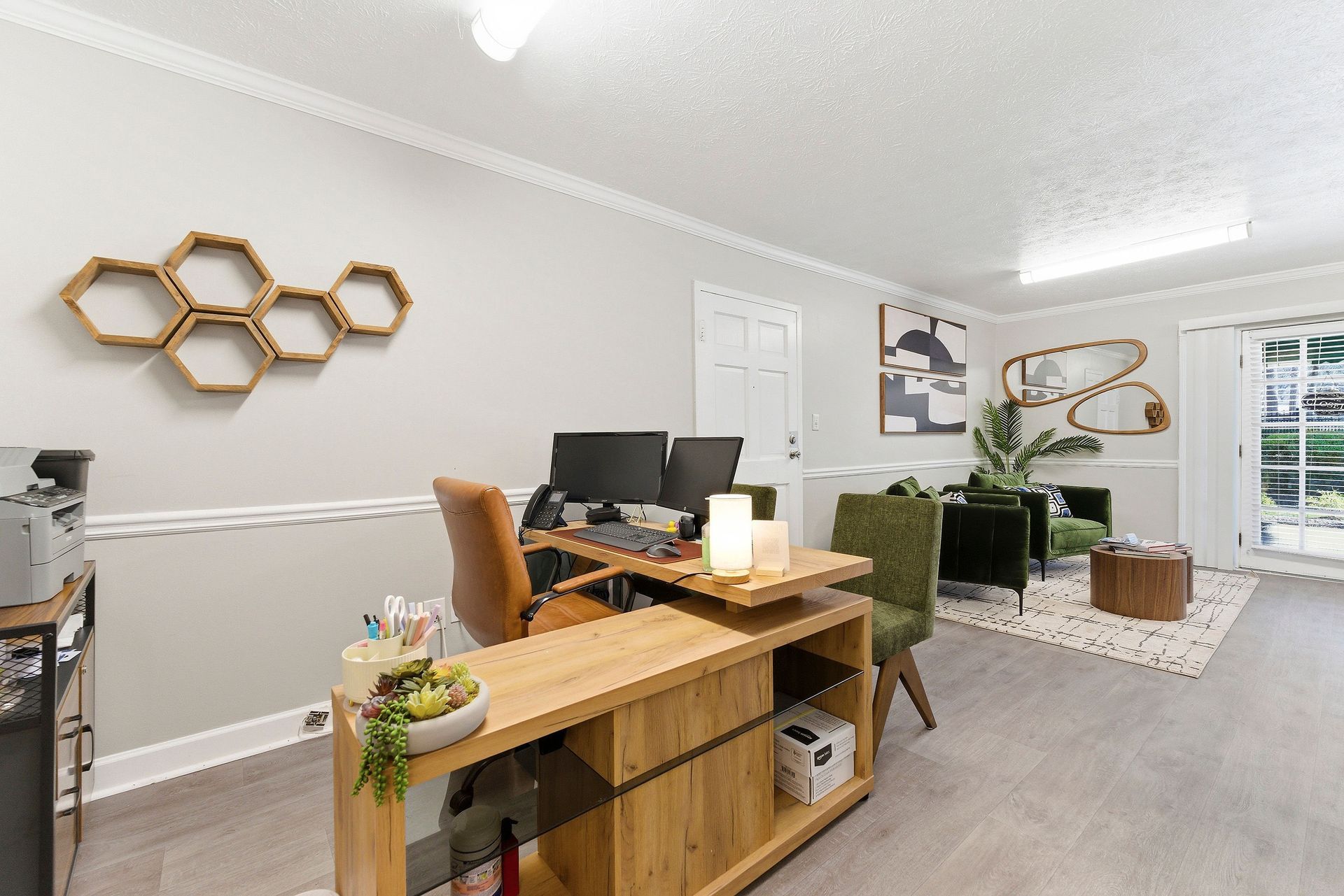 Modern office with desk, laptop, honeycomb wall art, plants, and a cozy seating area