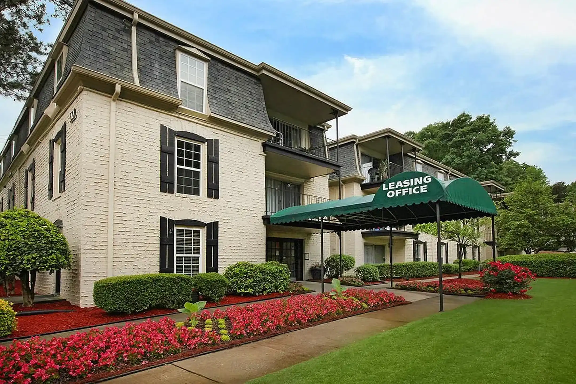 Two-story stone hotel with green awning, red flowers, and manicured lawn under a blue sky