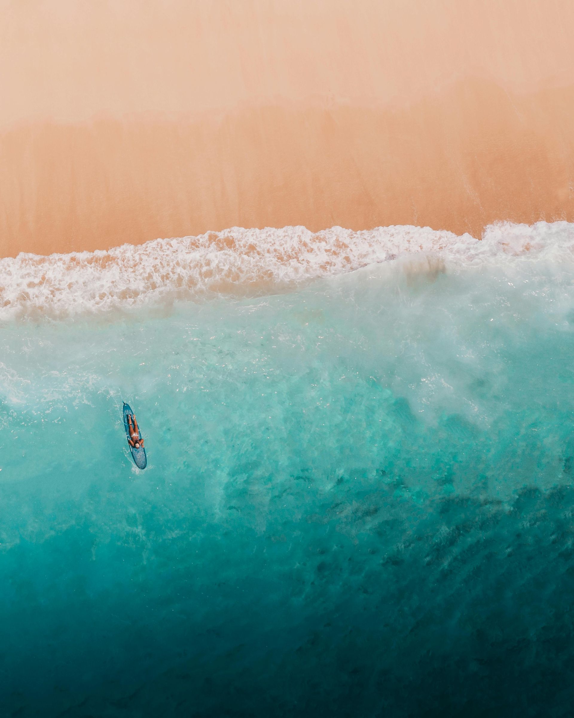 Ocean and a beach an aerial view of a person riding a wave on a surfboard in the ocean .