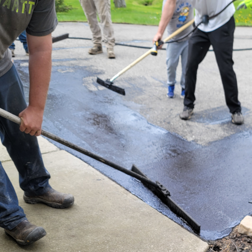 alpena asphalt armor's team in the process of sealcoating a driveway with squeegees