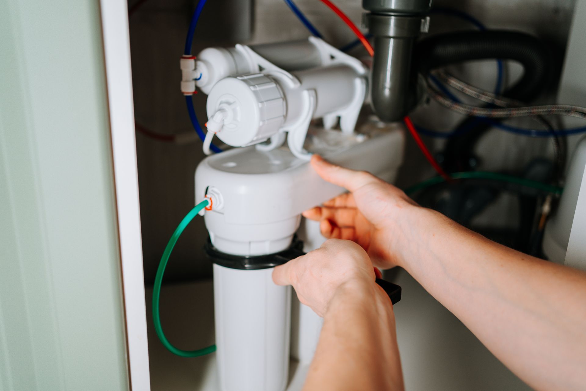 Hands adjusting a white water filter system under a sink with green tubing