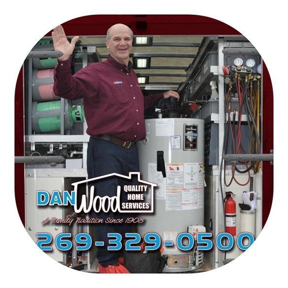 A man in a red shirt is standing next to a hot water heater