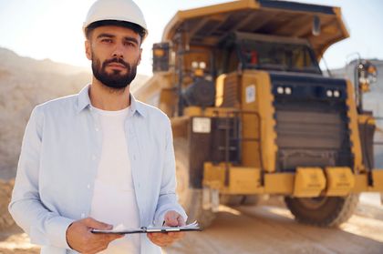 A man is standing in front of a dump truck holding a clipboard.