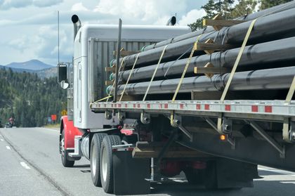 A semi truck is carrying a stack of pipes on the back of it.