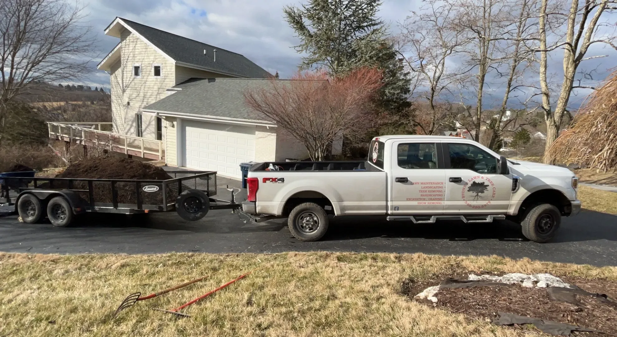 A white truck is towing a trailer with a house in the background.