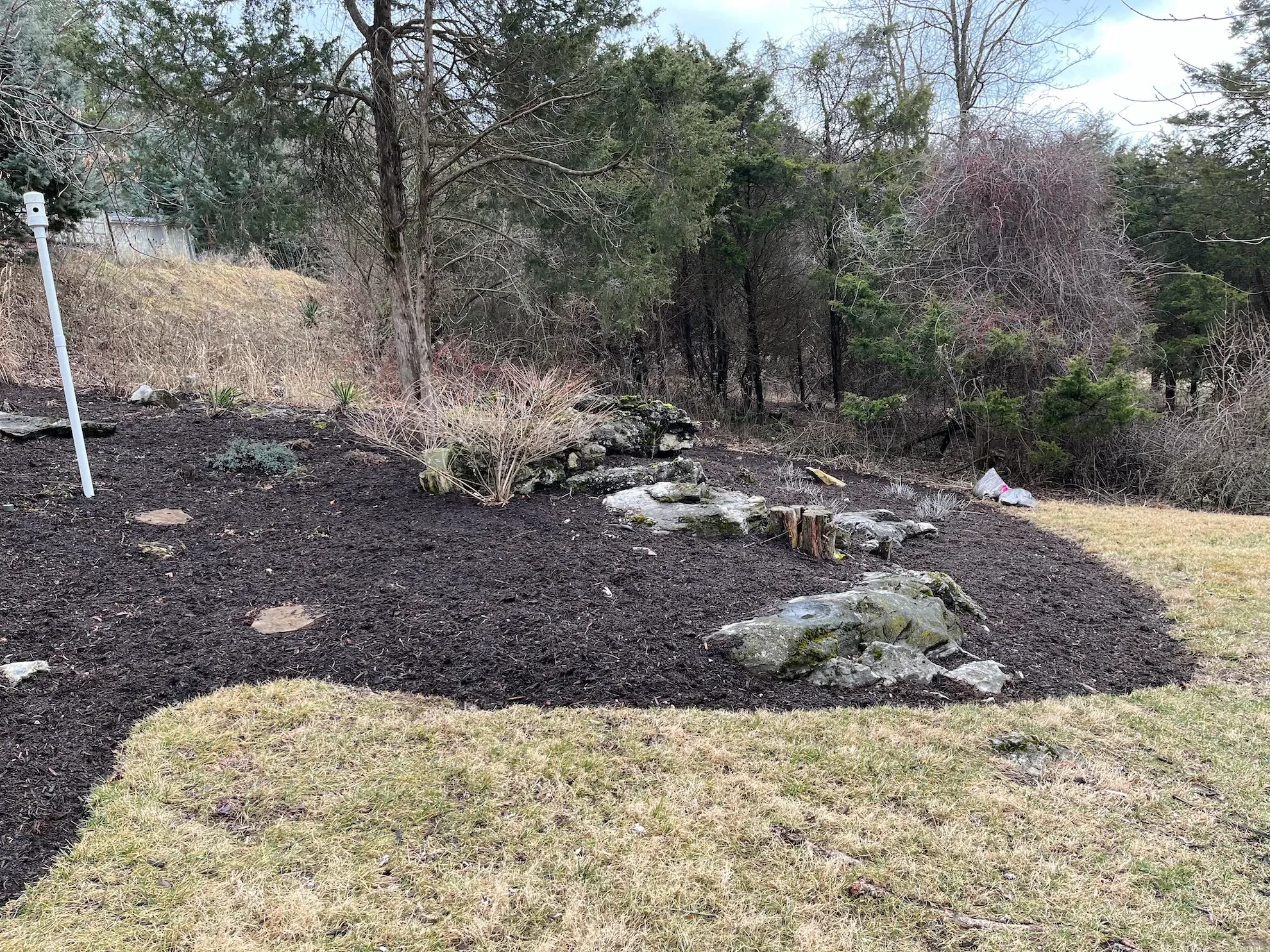 A yard with a lot of mulch and rocks in it and trees in the background.