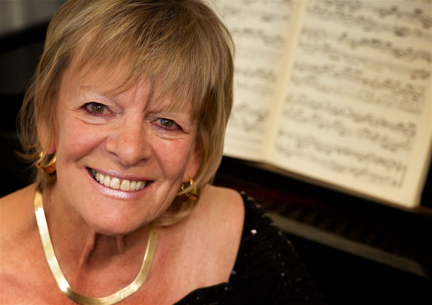 Close up head shot of Jacquelyn Helin sitting at a piano with sheet music in the background.
