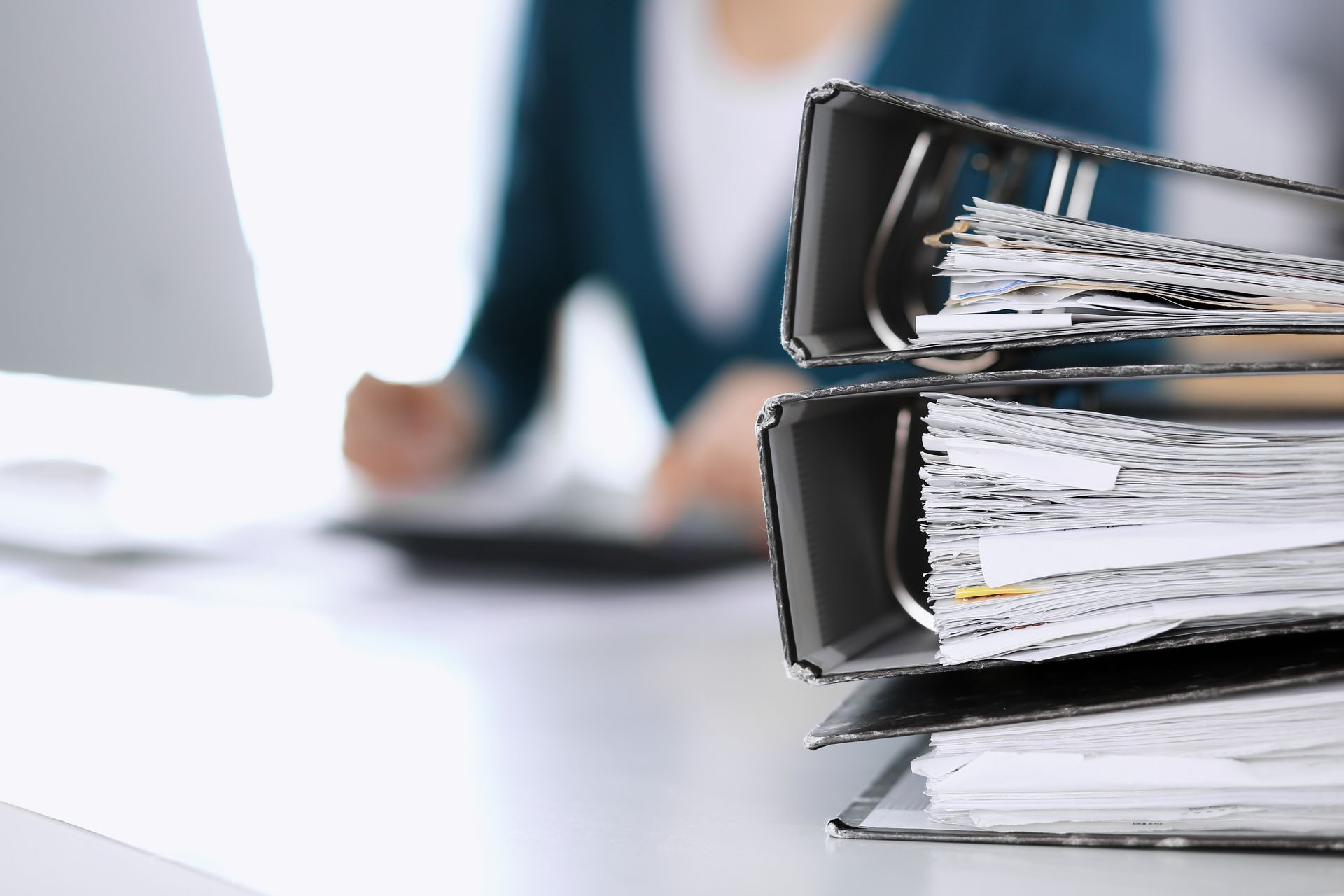 Stack of file binders on a desk with a person working in the background.