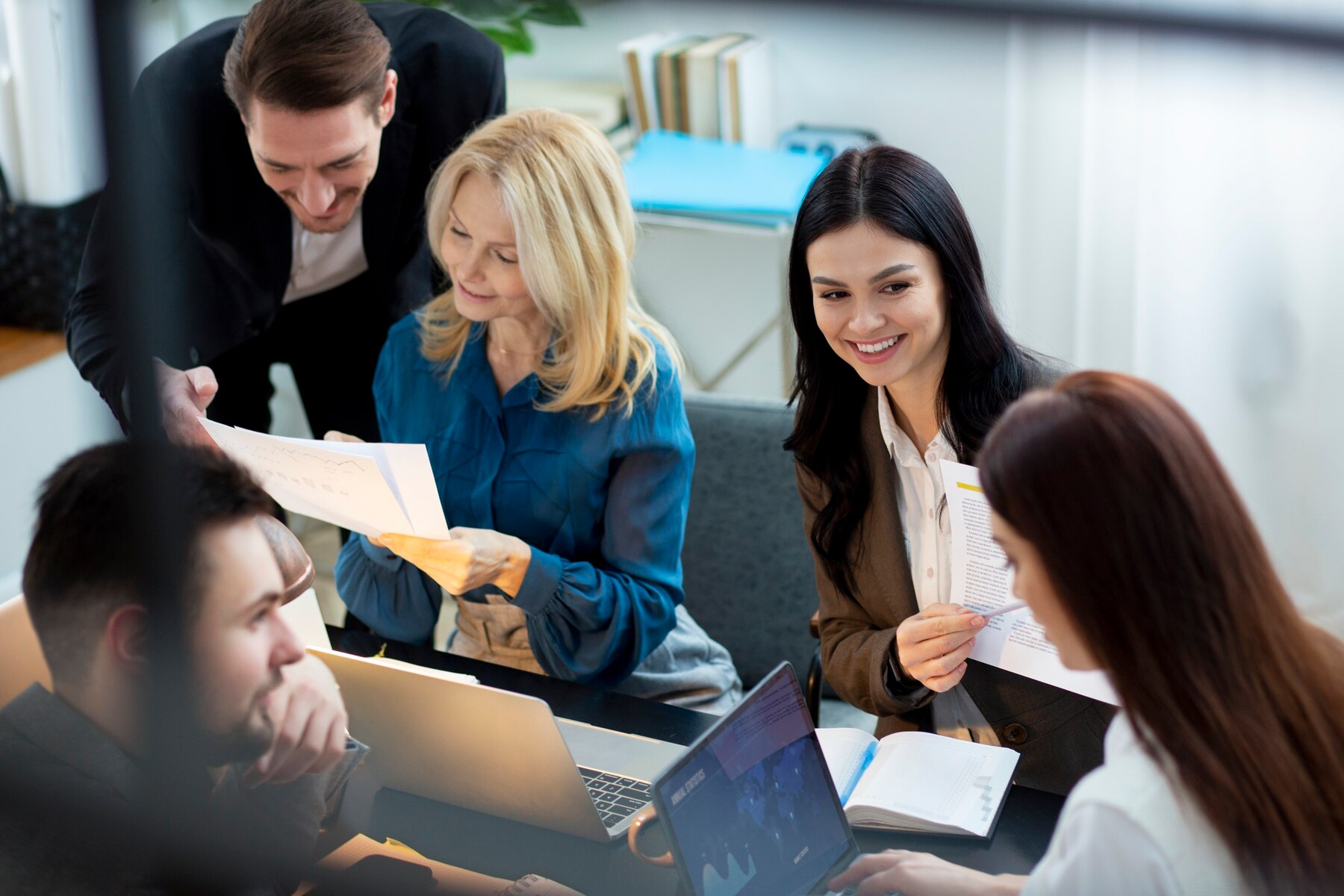 Business team collaborating, examining documents around a table in an office setting, smiling.