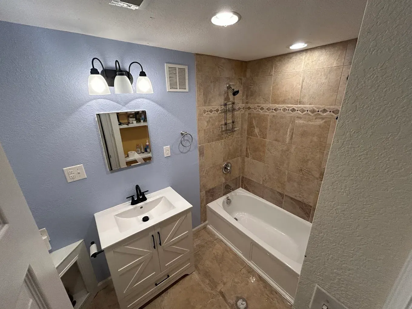Bathroom with blue walls, white vanity, and tiled shower/tub combo.