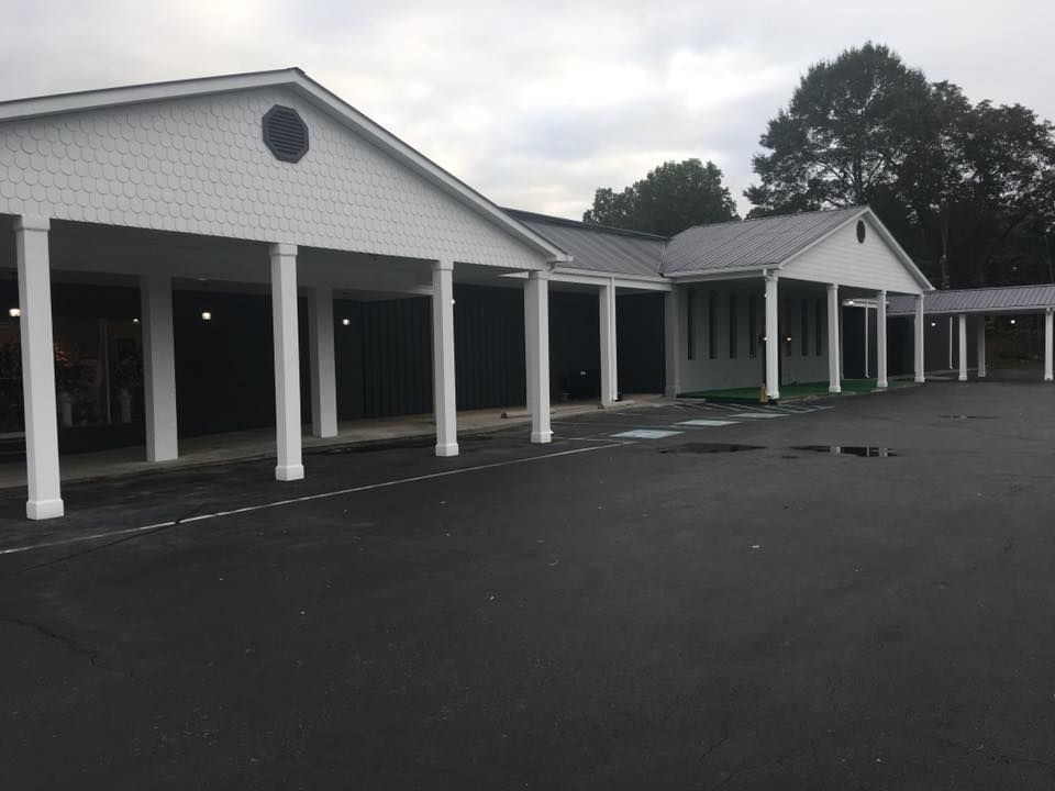 White building with covered walkways and columns beside an empty paved lot under cloudy skies