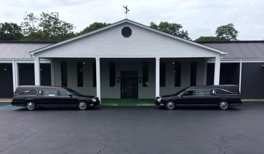 Two black limousines parked outside a white building with a green entrance and covered porch.