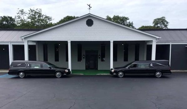 Two black limousines parked in front of a white building with a covered porch