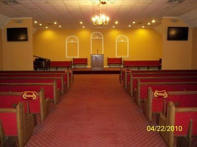 Empty church sanctuary with red pews, central aisle, and altar under warm ceiling lights