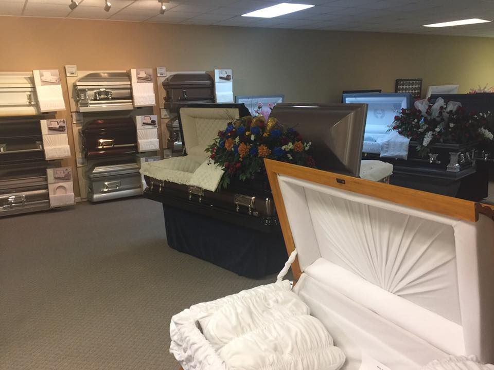 Open casket with white lining in a funeral home showroom, surrounded by caskets and floral arrangements