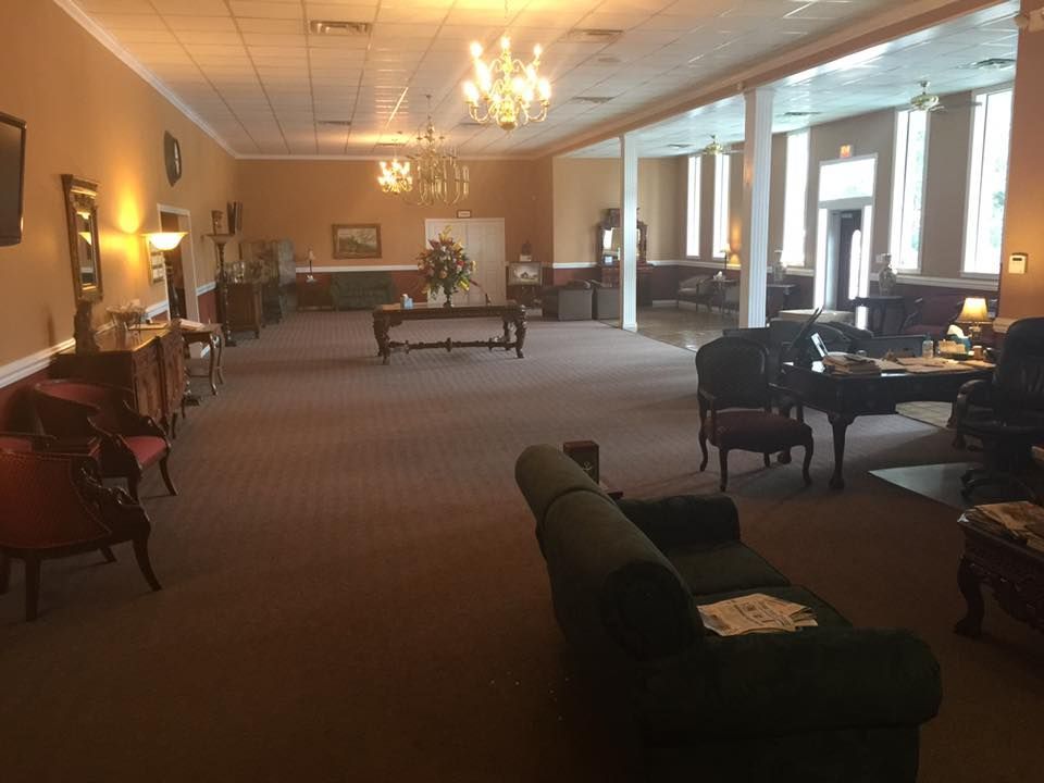 Elegant lounge with chandeliers, sofas, chairs, and large windows in a spacious carpeted room