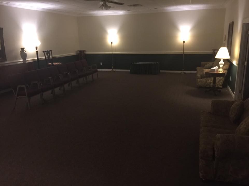 Empty dimly lit room with rows of chairs, wall sconces, and a lamp by a sofa