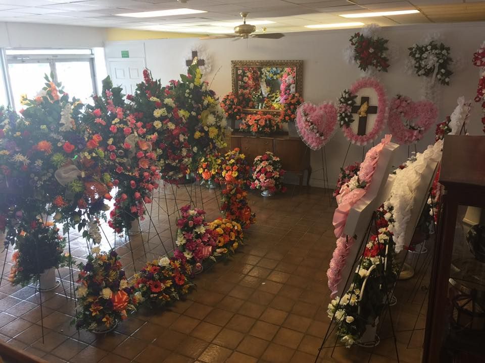 Indoor room filled with colorful floral arrangements and wreaths on a tiled floor.