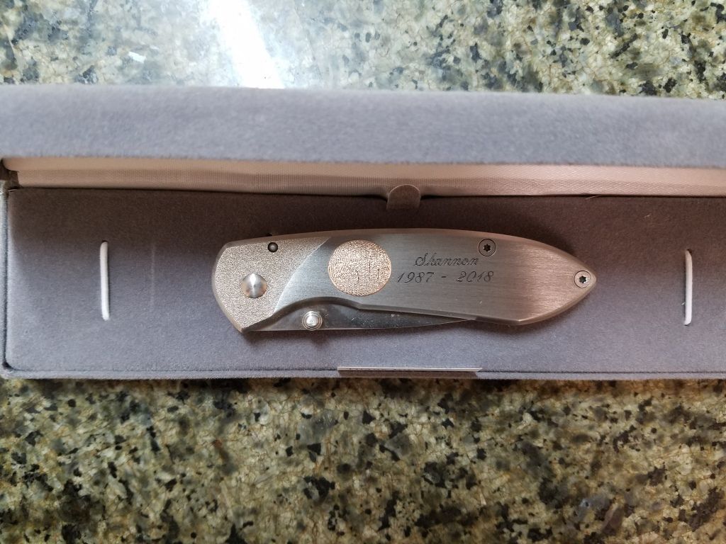 Small silver pocket knife in a foam-lined box on a speckled countertop.