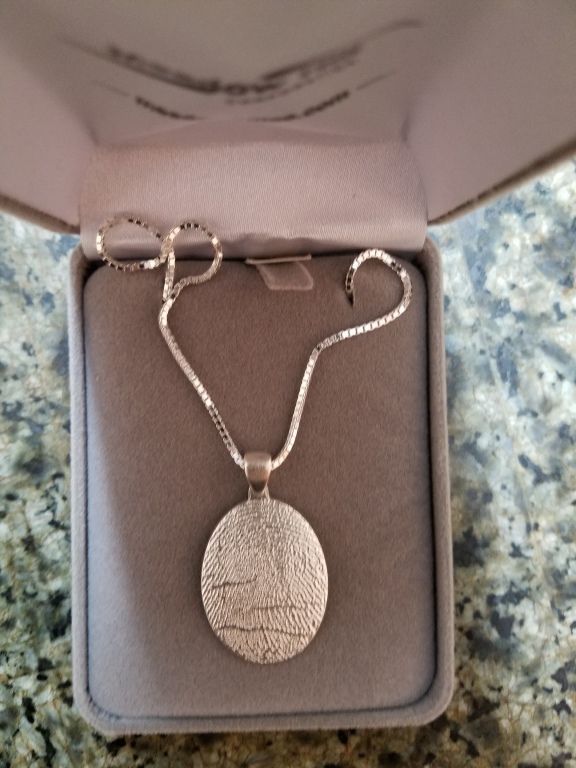 Silver necklace with an oval pendant in a gray jewelry box on a speckled countertop