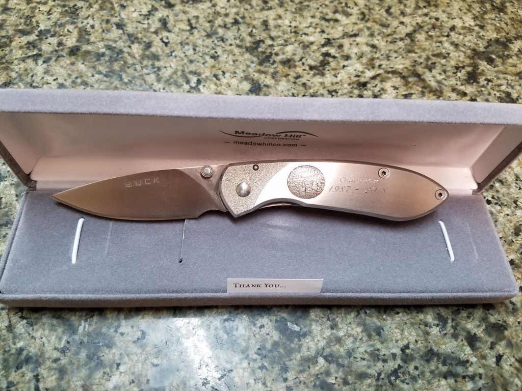 Bronze folding knife displayed in a blue box on a speckled countertop