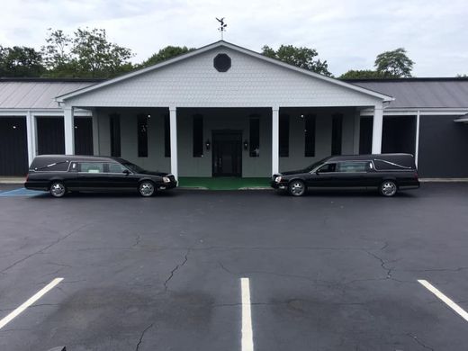 Front view of a white building with a covered entrance and two black limousines parked out front